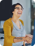 Smiling person with glasses and short hair wearing a mustard cardigan shaking hands.