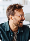 Smiling man with glasses and beard wearing a green button-up shirt.