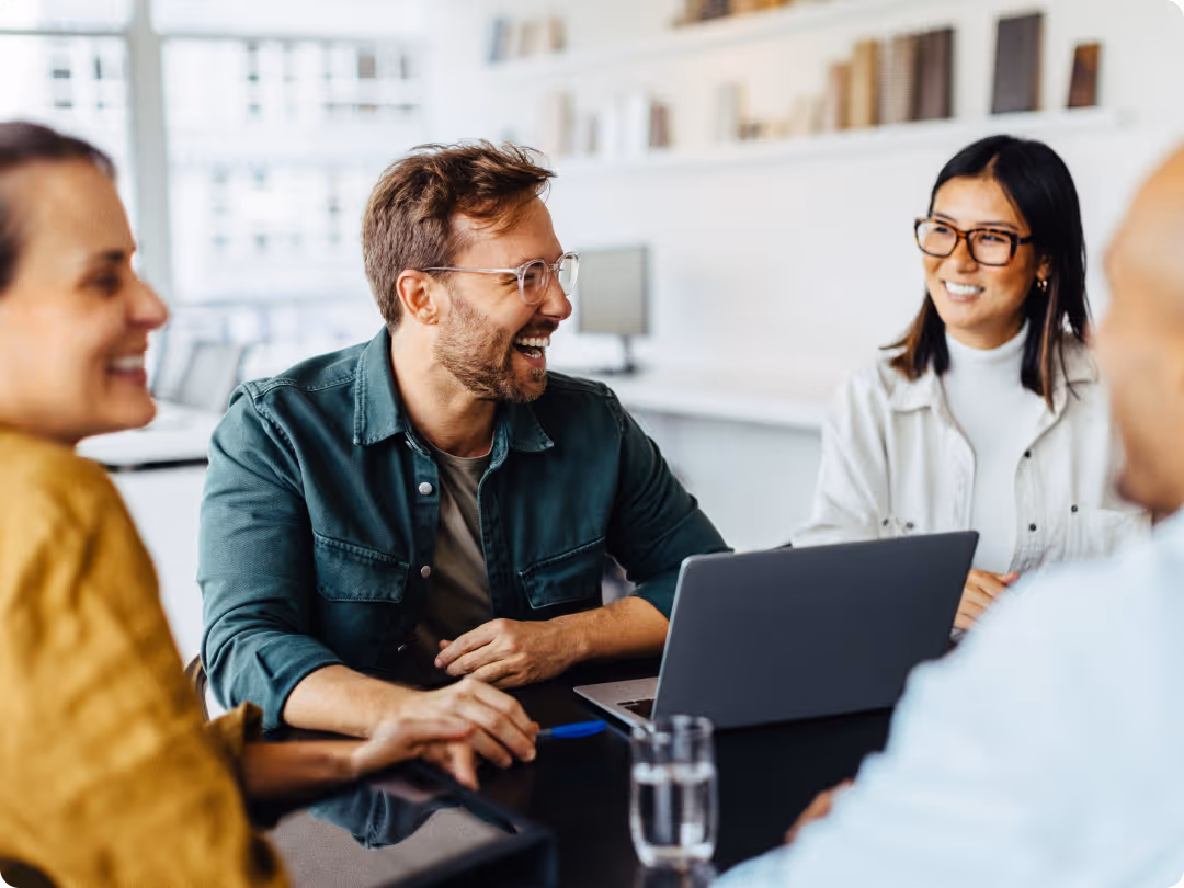 Smiling young professionals sitting around a table with a laptop, having a meeting in an office.