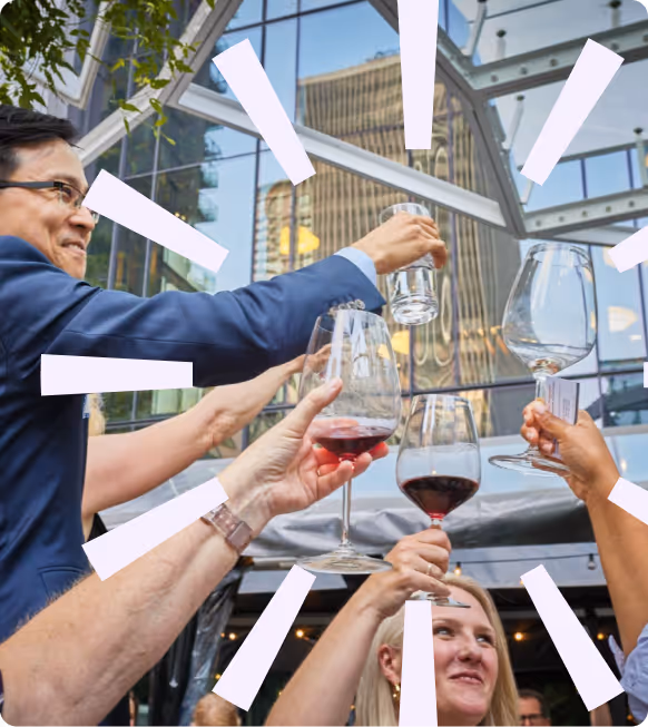 People raising glasses in a toast outdoors by a glass building with a cityscape reflection.