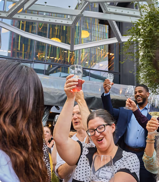 Group of people raising glasses and toasting in a lively outdoor urban setting.