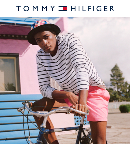 model sitting on a bicycle with pink shorts, plaid bucket had and striped long sleeve.