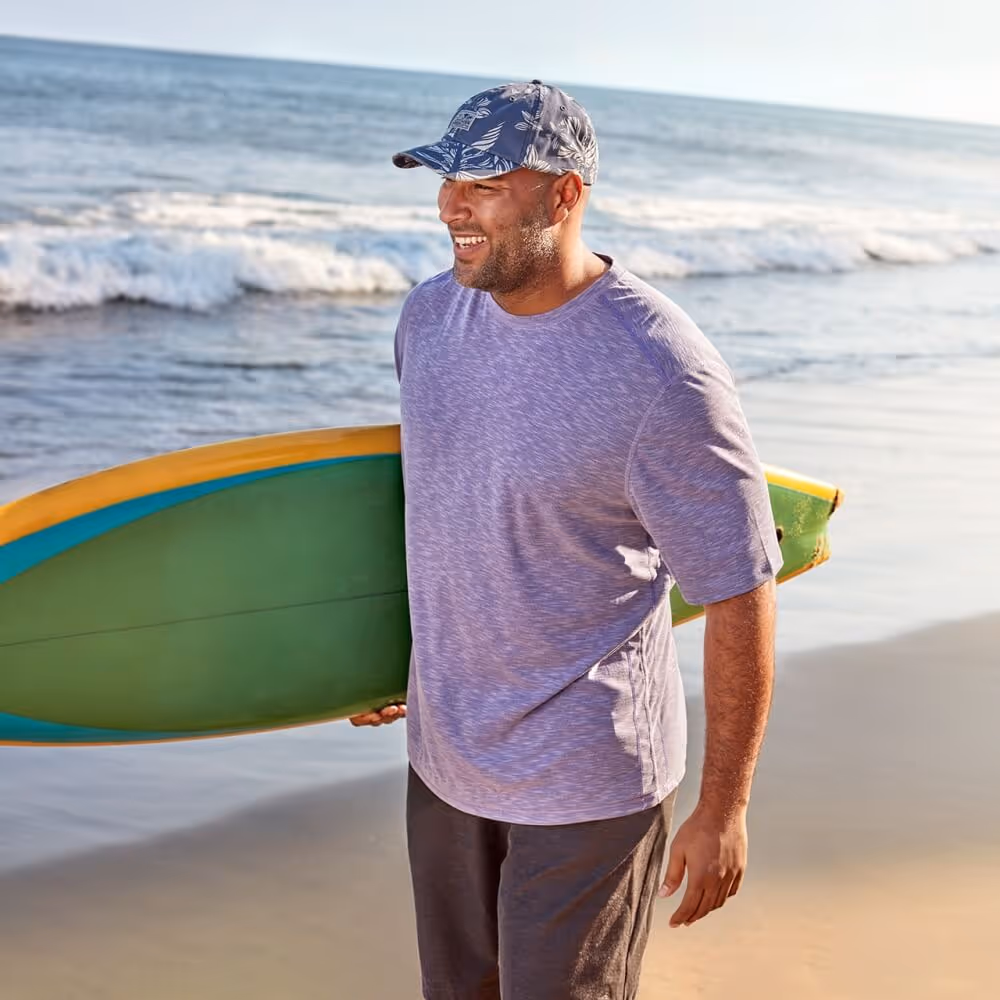 Man wearing Tommy Bahama clothing holding a surfboard on the beach