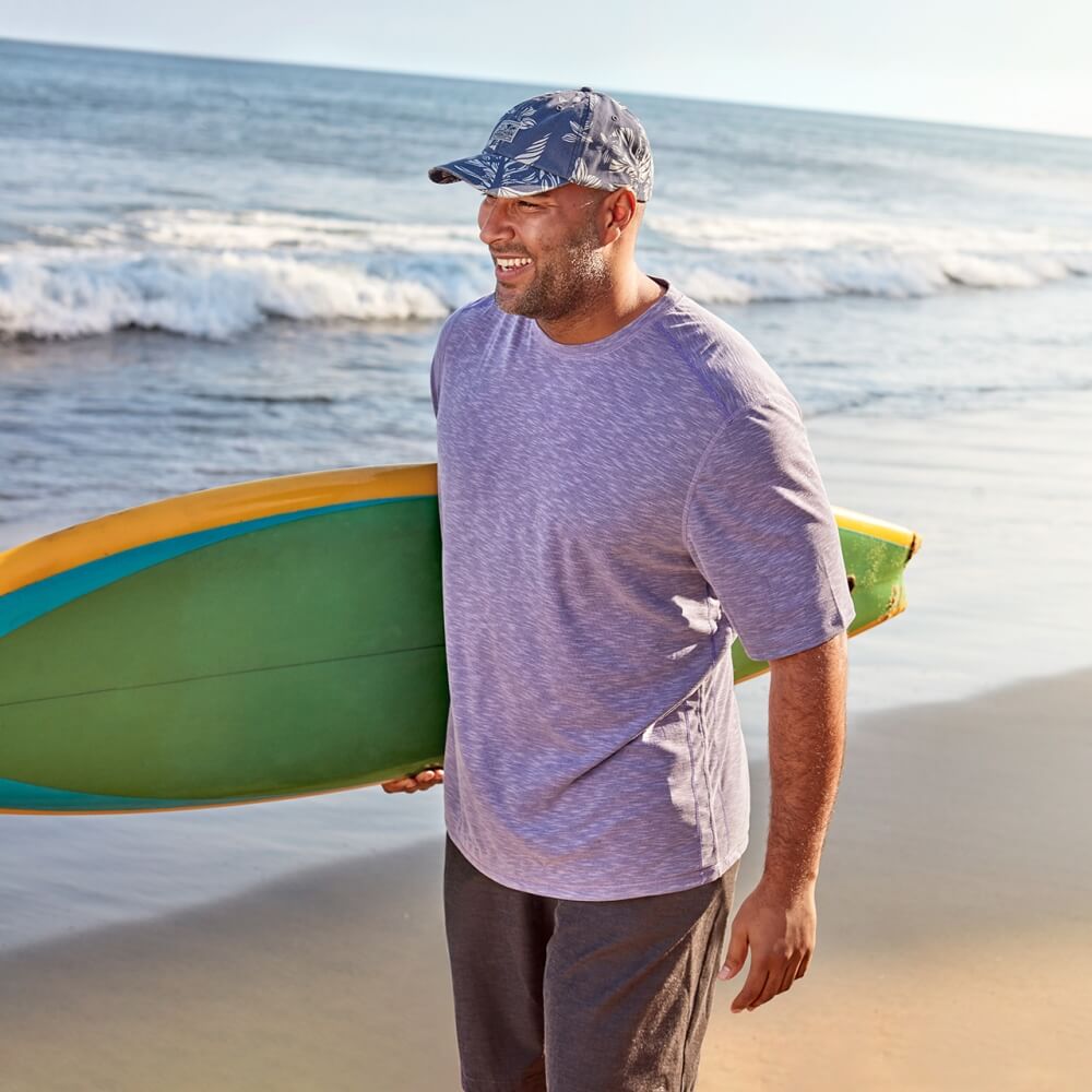 Man wearing Tommy Bahama clothing holding a surfboard on the beach