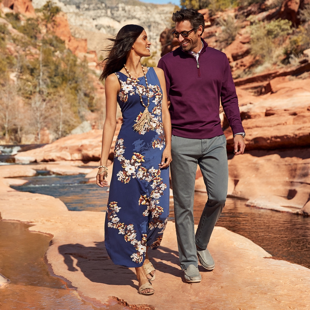 female model with tommy bahama dress and male model with jeans and maroon longsleeve walking in an orange rocky dessert by a stream 