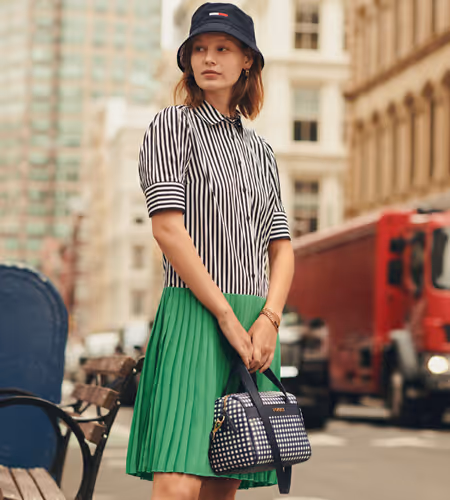 Young woman wearing a Tommy Hilfiger bucket hat, handbag, black and white striped shirt, and bright green skirt on the street