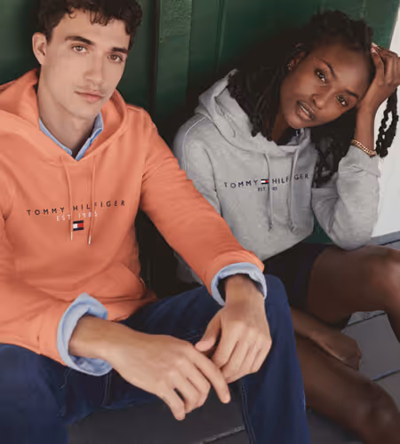 Young man wearing a salmon-colored Tommy Hilfiger sweater and a young woman wearing a gray Tommy Hilfiger Sweater