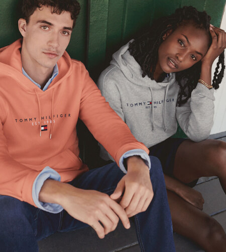 Young man wearing a salmon-colored Tommy Hilfiger sweater and a young woman wearing a gray Tommy Hilfiger Sweater