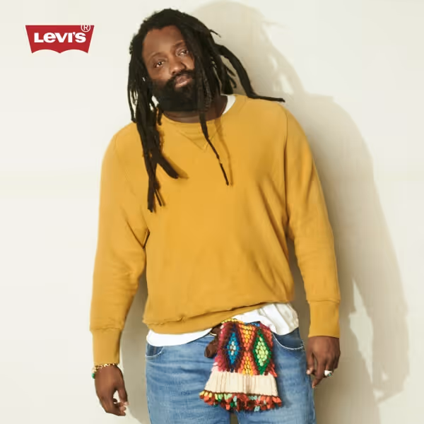Man wearing a mustard-colored Levi's sweater, jeans, and a colorful scarf around his waist