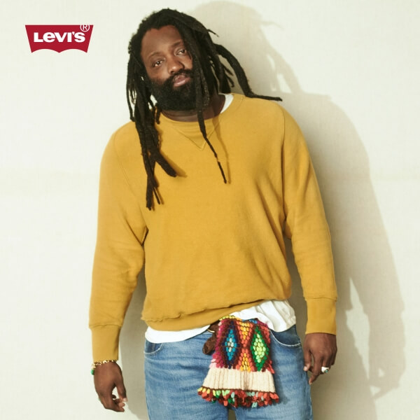 Man wearing a mustard-colored Levi's sweater, jeans, and a colorful scarf around his waist