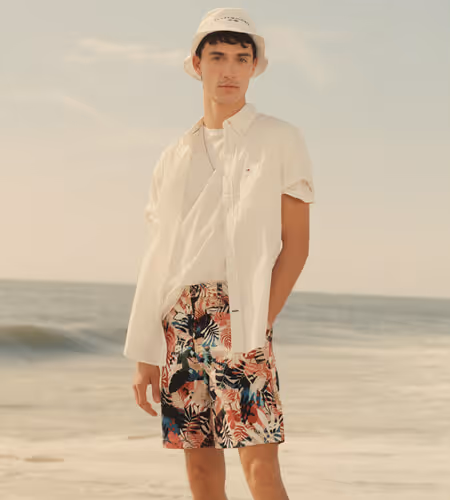 Young man on a beach wearing Tommy Hilfiger white shirt and bucket hat with tropical print shorts