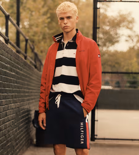 Young man wearing Tommy Hilfiger red sweater, black and white striped shirt, and navy blue swim shorts