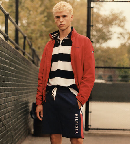 Young man wearing Tommy Hilfiger red sweater, black and white striped shirt, and navy blue swim shorts