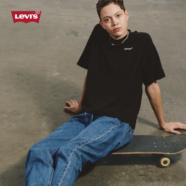 Model wearing Levi's black t-shirt and denim jeans while sitting on a skateboard
