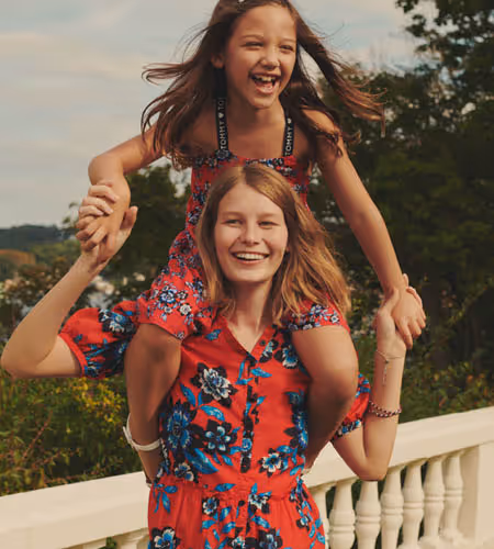 Woman in a floral red Tommy Hilfiger dress holding her daughter on her shoulders