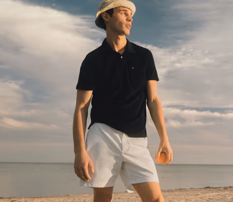 Young man wearing Tommy Hilfiger Black collared short-sleeve shirt, white shorts, and tan bucket hat. 