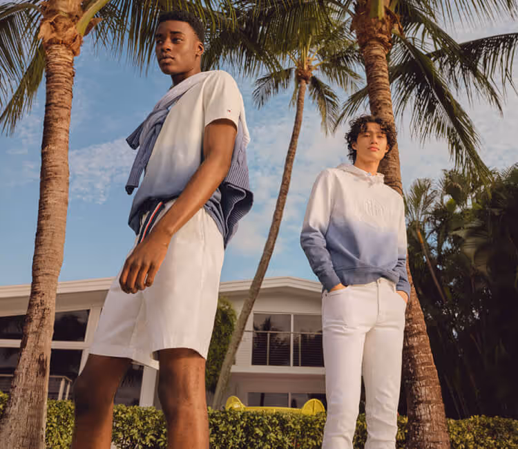 Two young men wearing Tommy Hilfiger blue and white gradient sweaters; one with white shorts and the other with white pants