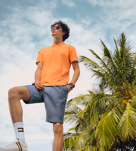 Young man wearing Tommy Hilfiger orange polo shirt and blue shorts
