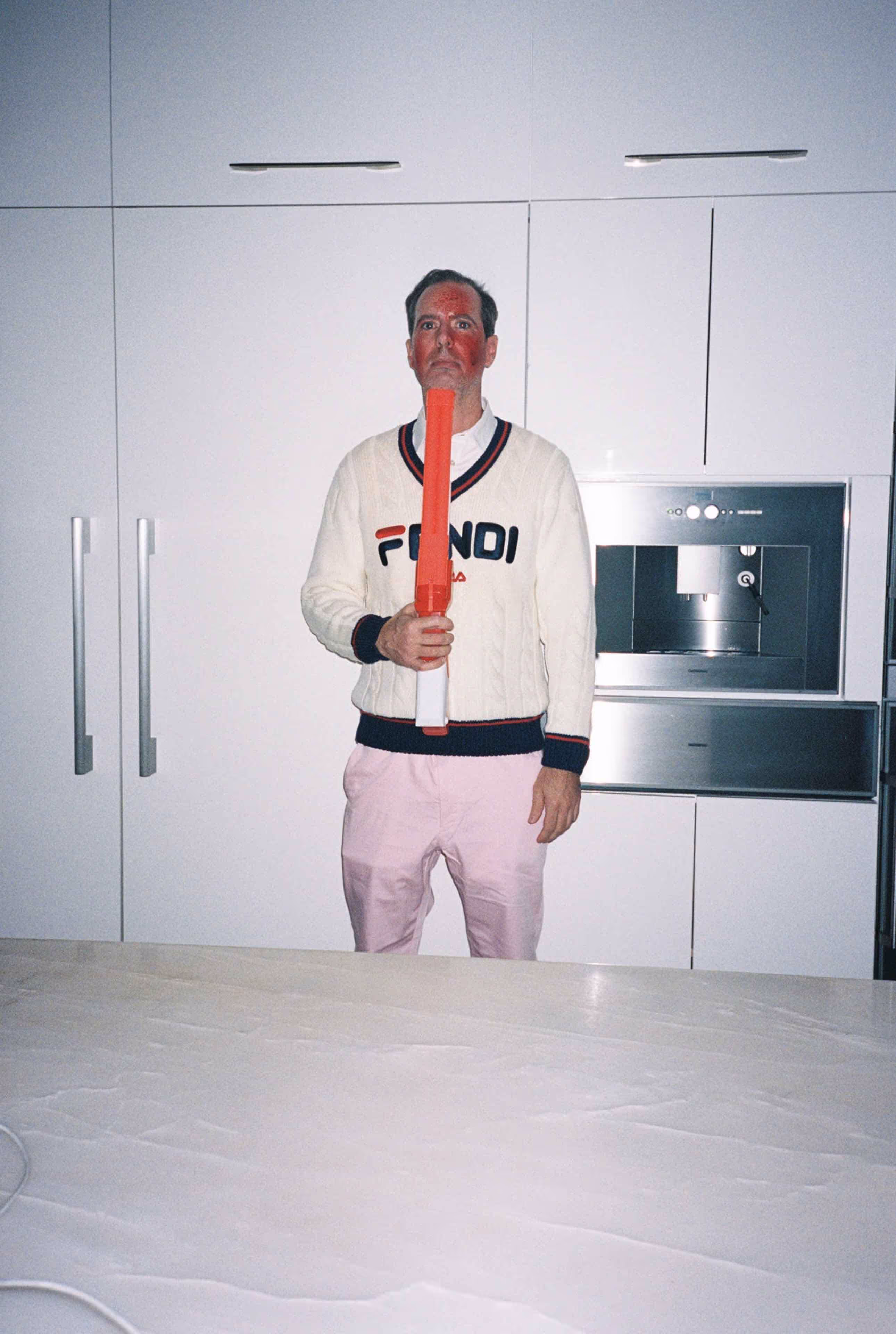 A man standing in a kitchen with a tie around his neck.