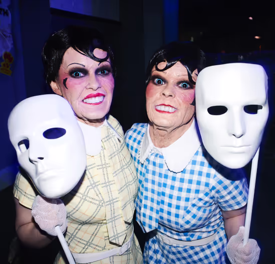 A couple of women standing next to each other holding masks.