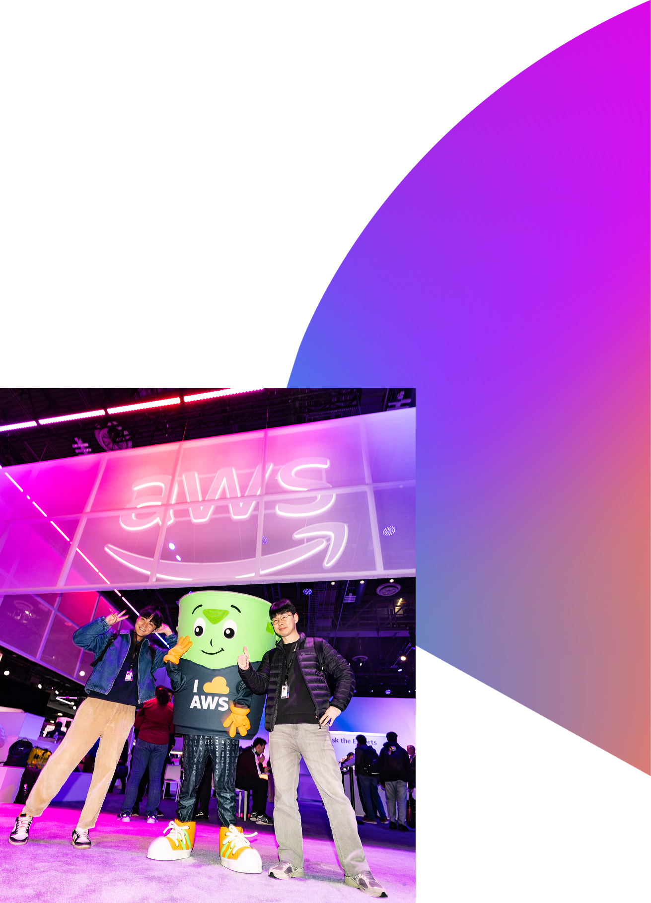 Two young men posing with a green AWS mascot wearing an 'I ❤️ AWS' shirt at a tech event with purple lighting.
