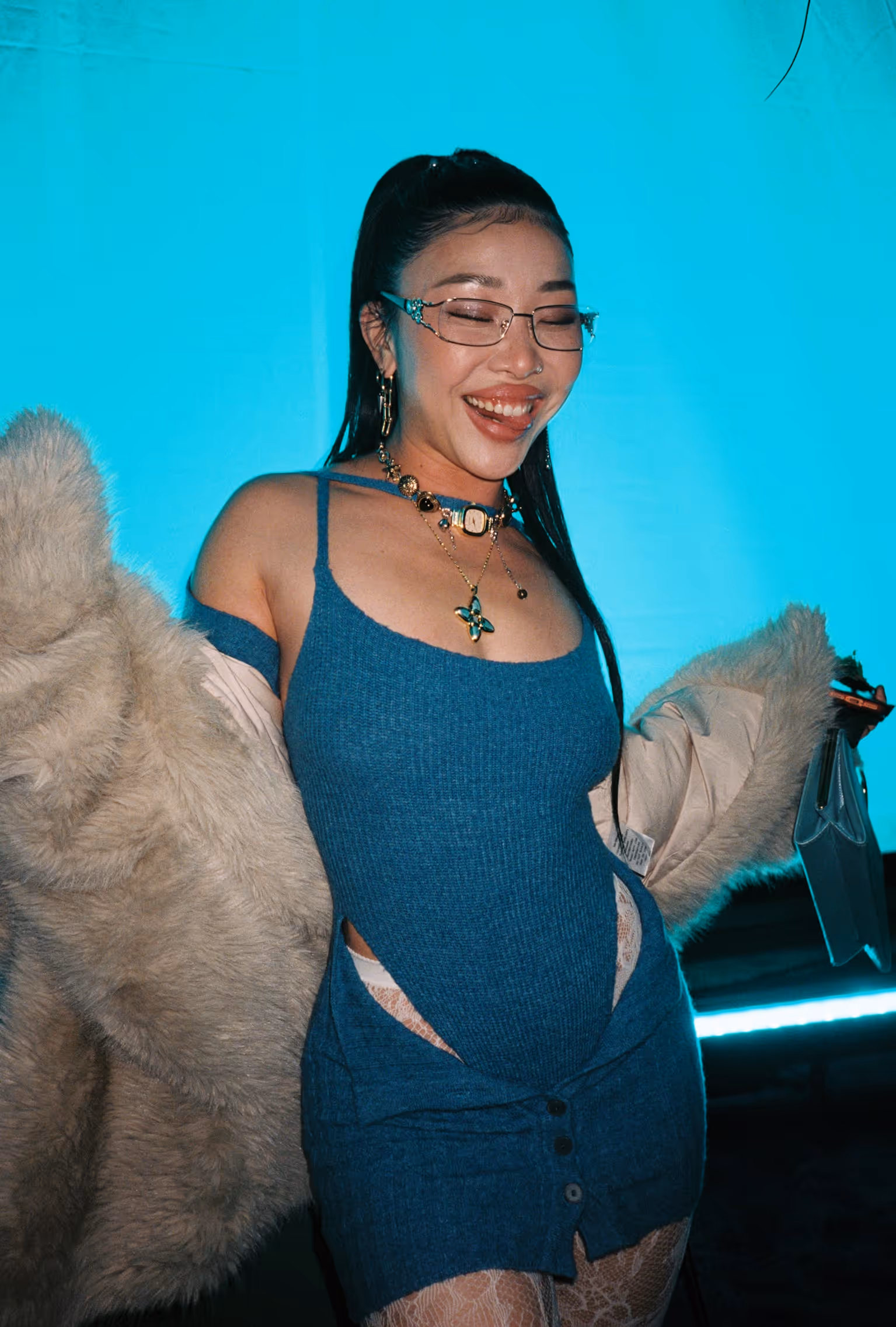 A woman in a blue dress and brown coat standing in front of a blue wall