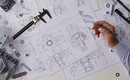 A picture of a person's hand holding a pen on top of engineering drawings signifying the Engineering & Technical category of Independent Professionals on Equilink
