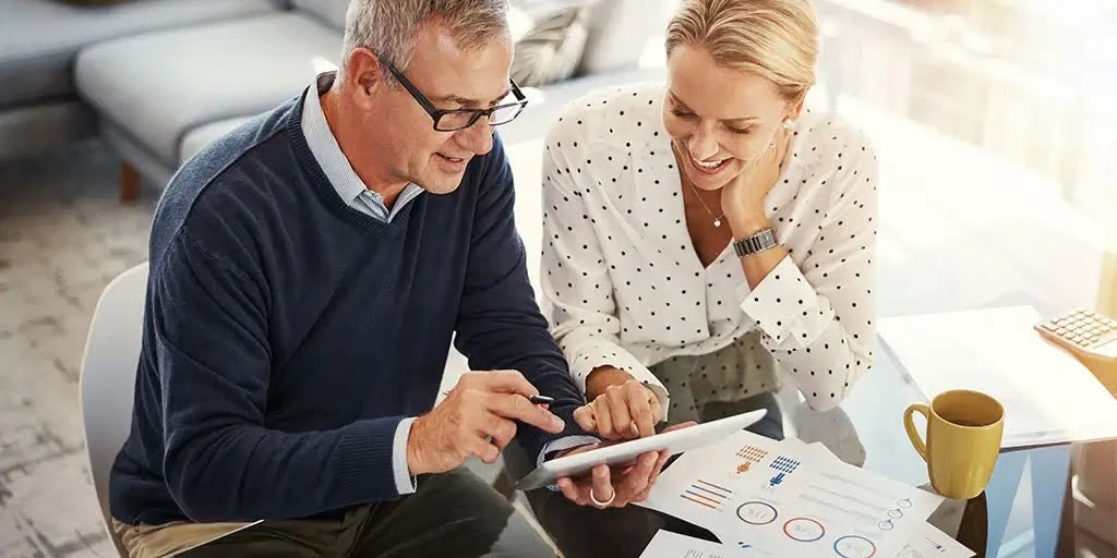 Man and woman sitting at a desk reviewing charts on a tablet.