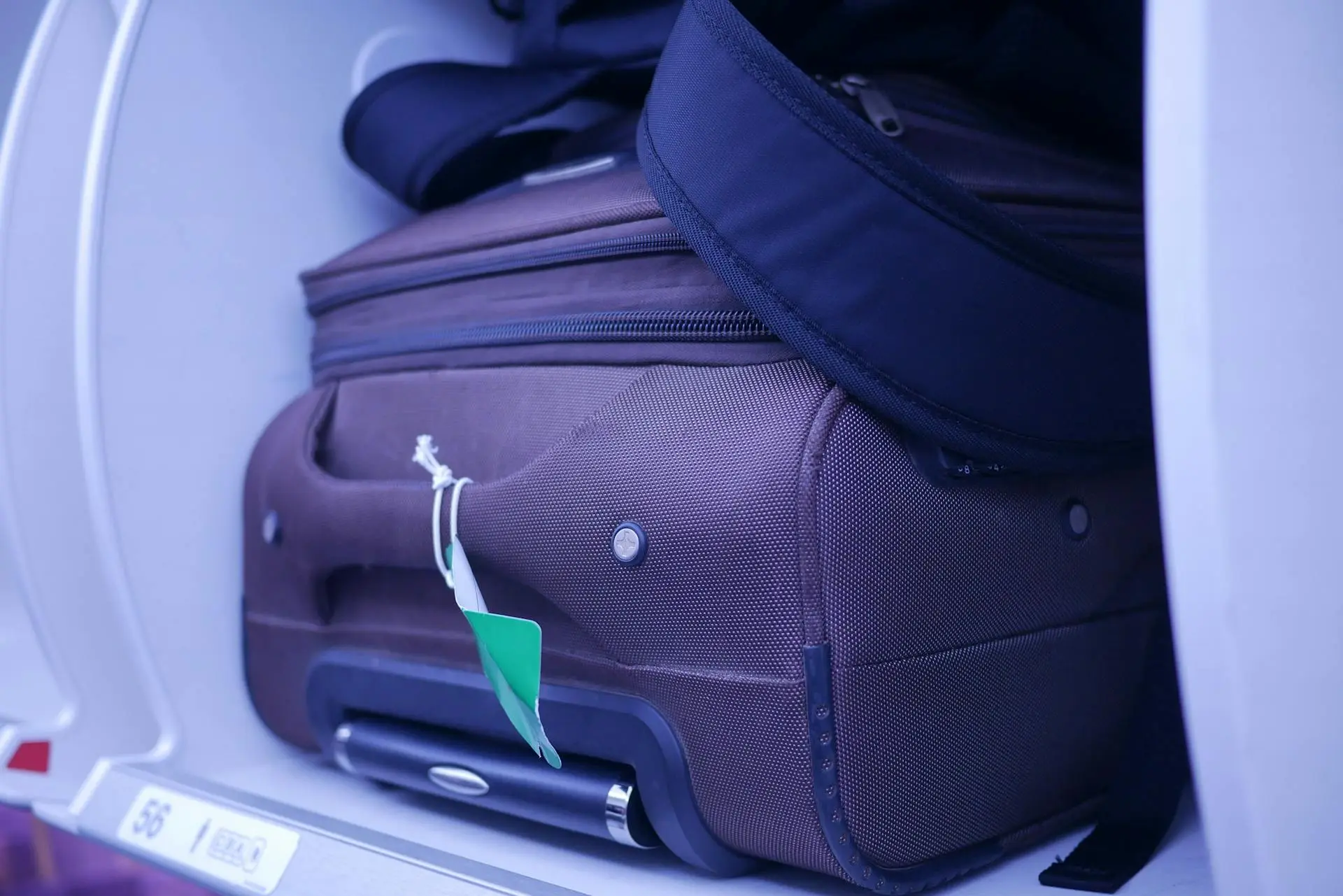 Brown suitcase with a green tag stored in an airplane overhead compartment