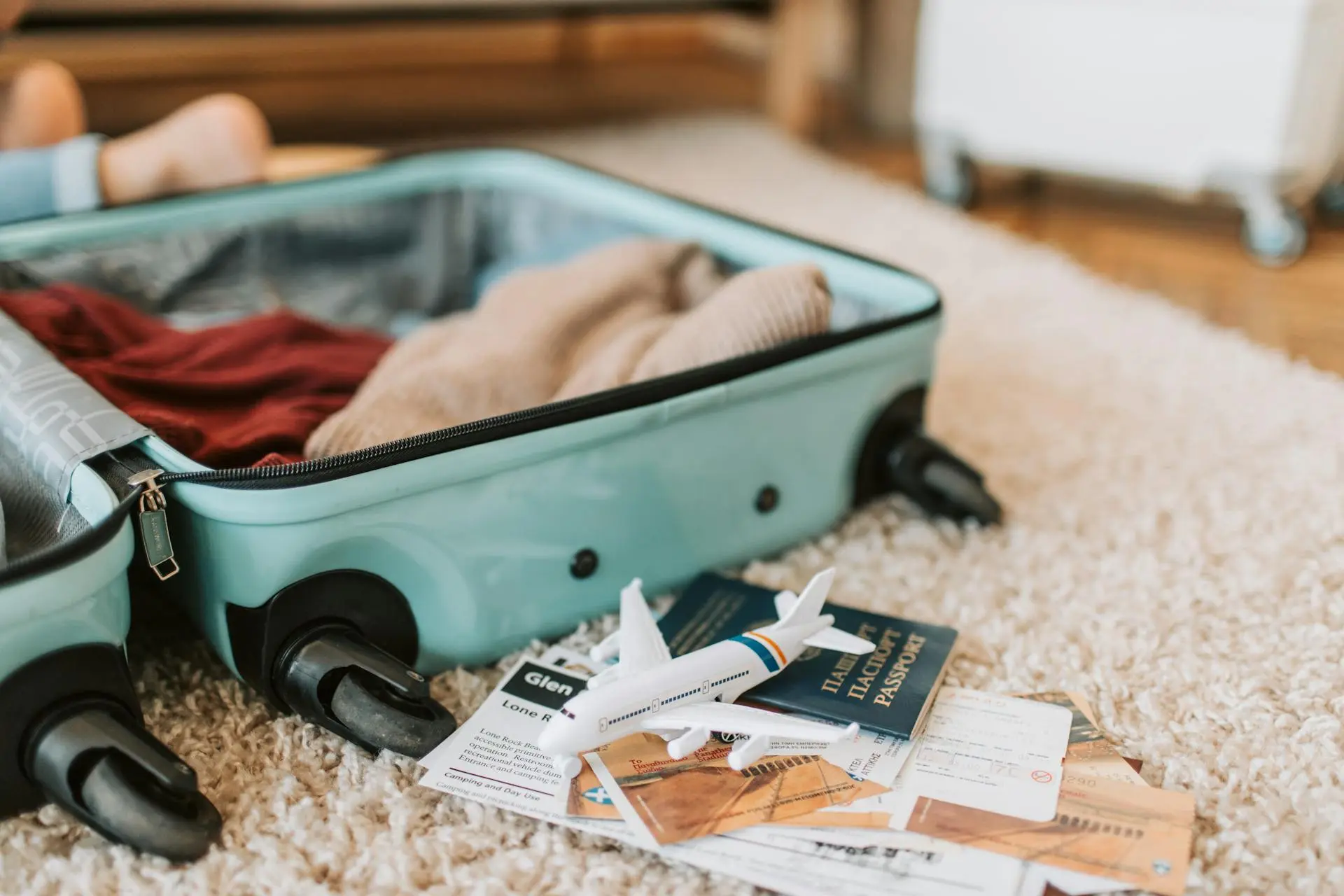 Open suitcase with clothes on a carpet, surrounded by passports, tickets, and a toy airplane