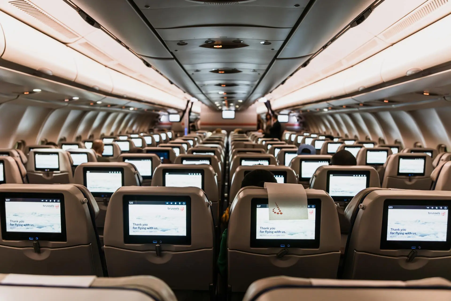 Airplane interior with rows of seats and seatback screens displaying welcome messages