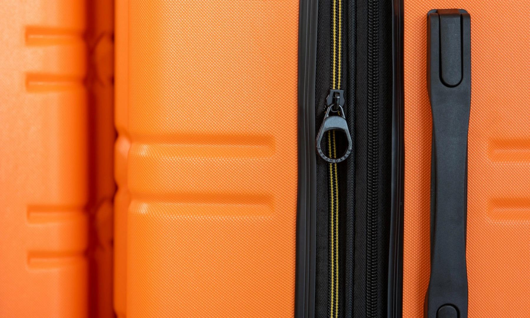 A close-up of the zip on a durable, bright orange suitcase.