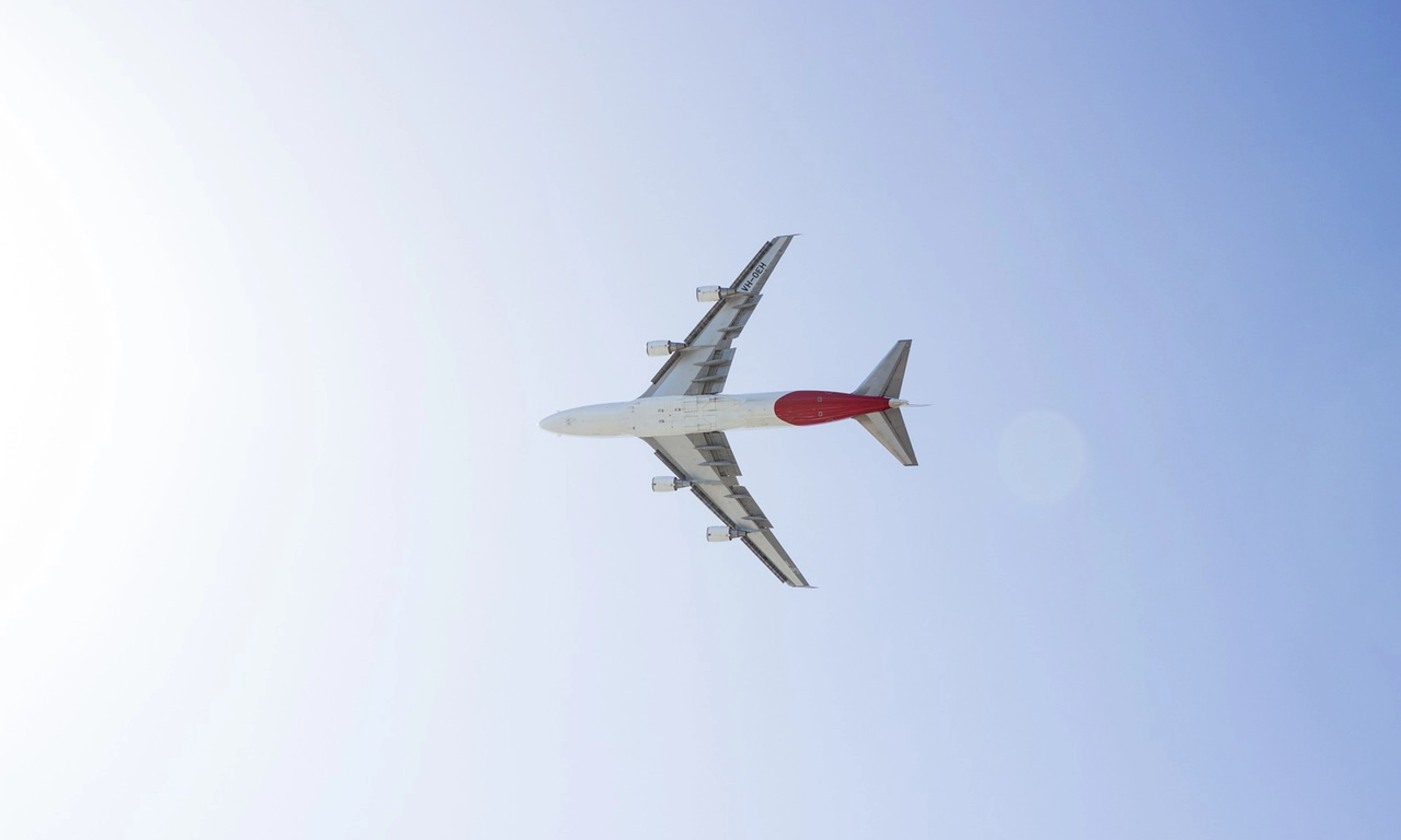 A large commercial aeroplane viewed from below as it flies overhead against a bright blue sky.