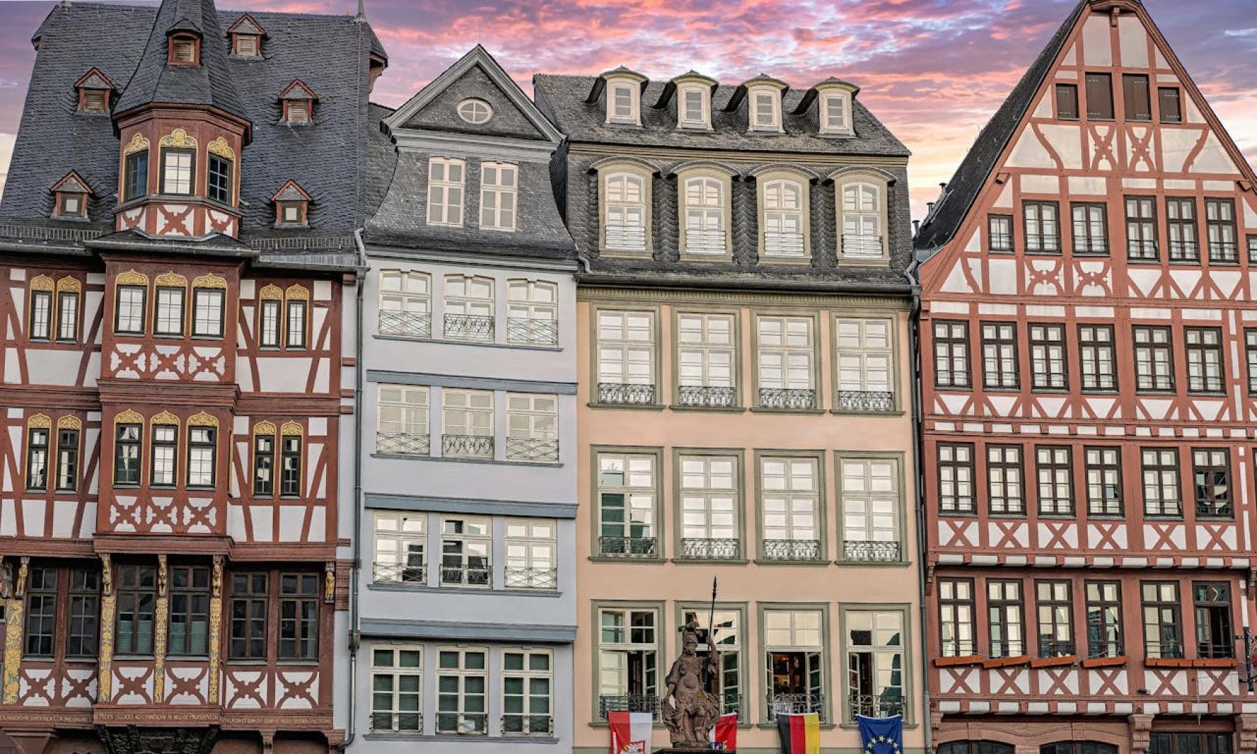 Colourful traditional German buildings in Frankfurt's Römer Square, featuring intricate half-timbered architecture with a pink and blue evening sky in the background.