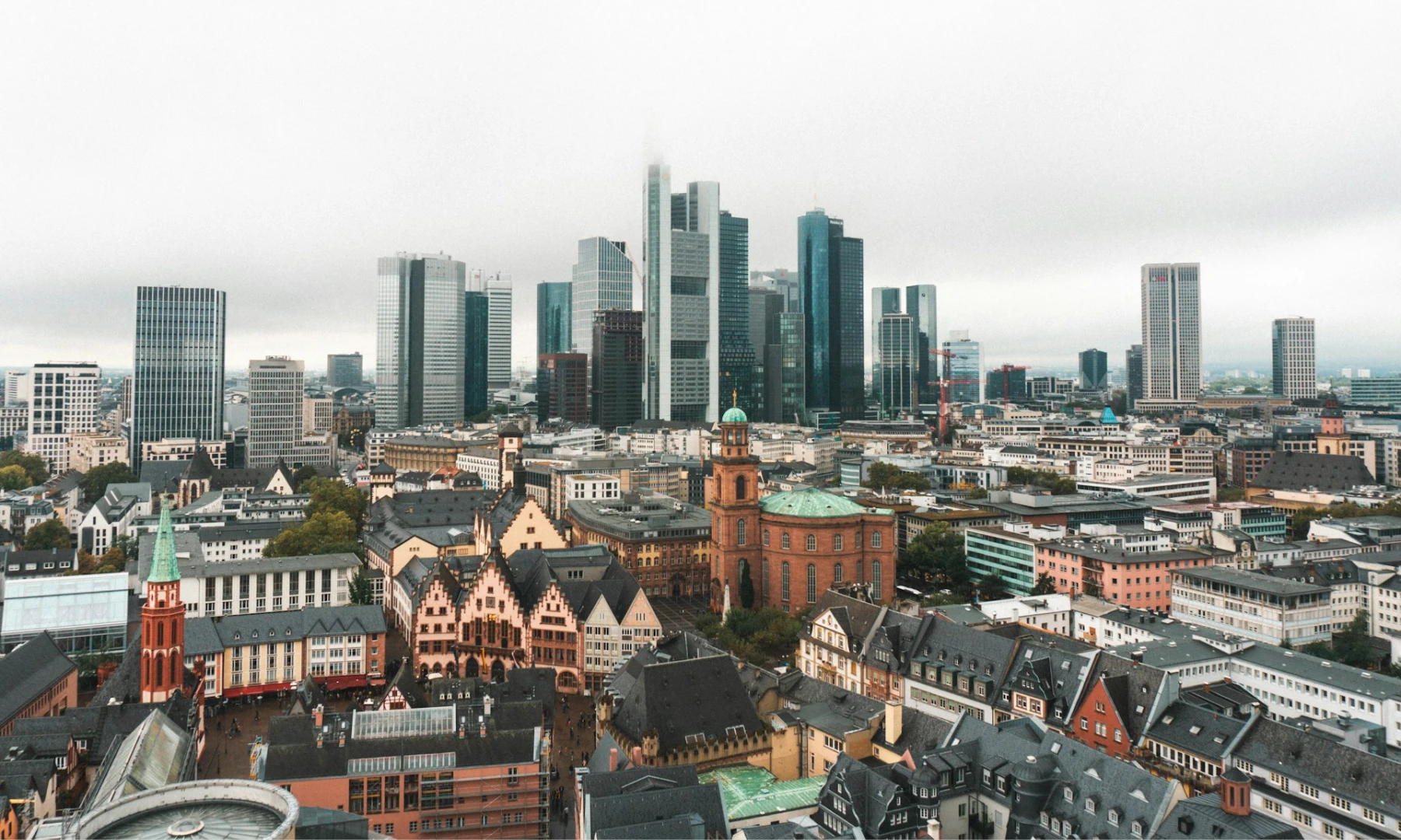Aerial view of Frankfurt, showcasing a mix of historic buildings in Römer Square and modern skyscrapers, under a cloudy sky.