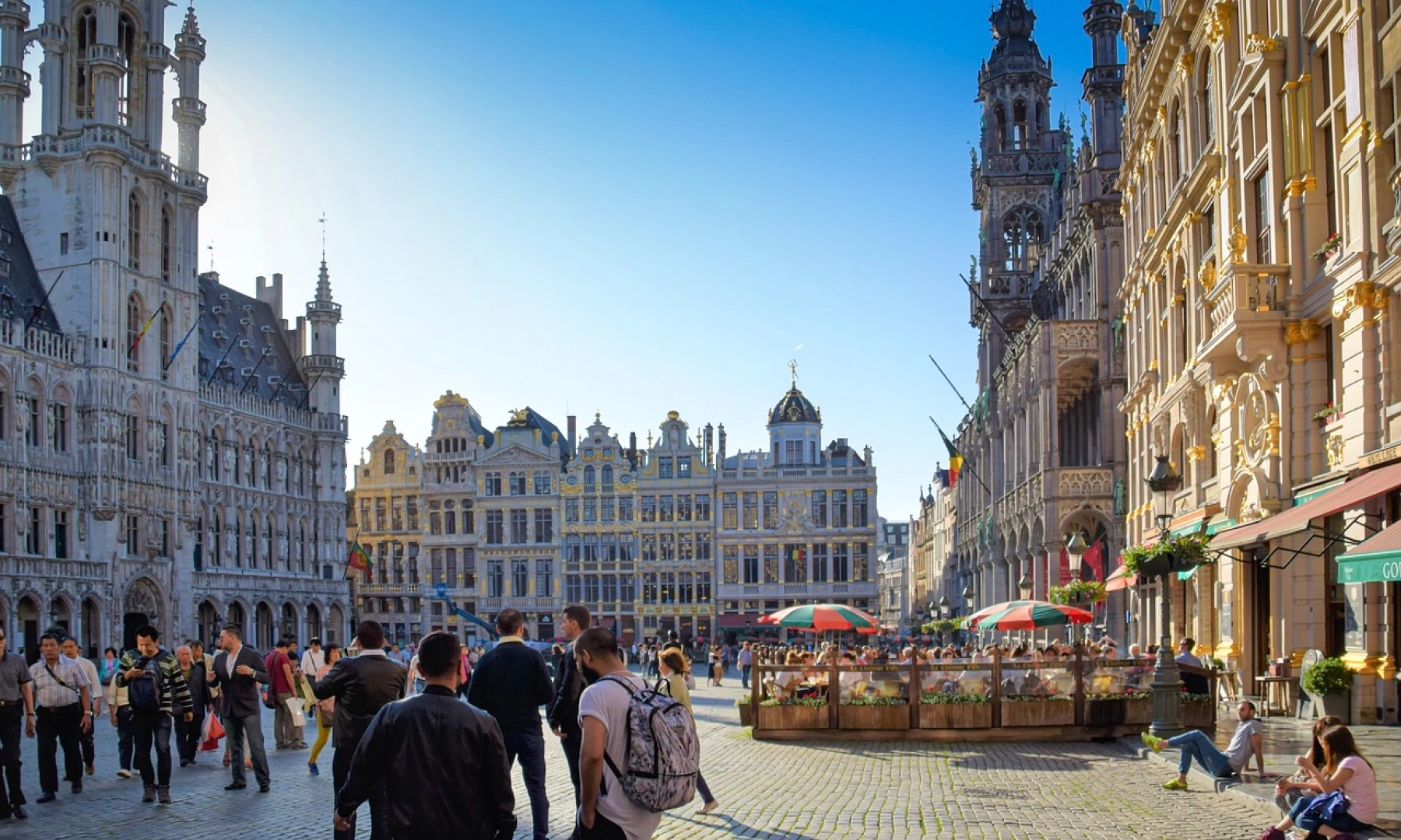The Grand Place in Brussels, Belgium, with its ornate guildhalls and the gothic-style Town Hall, bustling with people enjoying the sunny day.