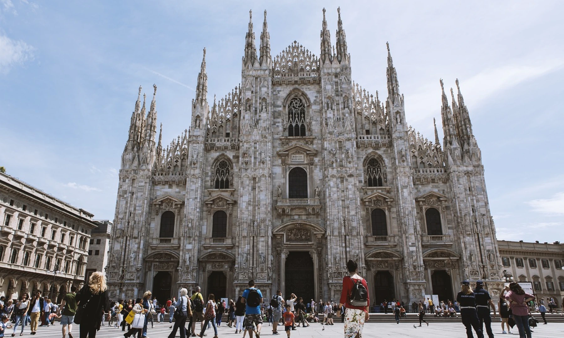 The Milan Cathedral (Duomo di Milano) in Italy, showcasing its intricate Gothic architecture, with tourists and locals walking around the square in front.