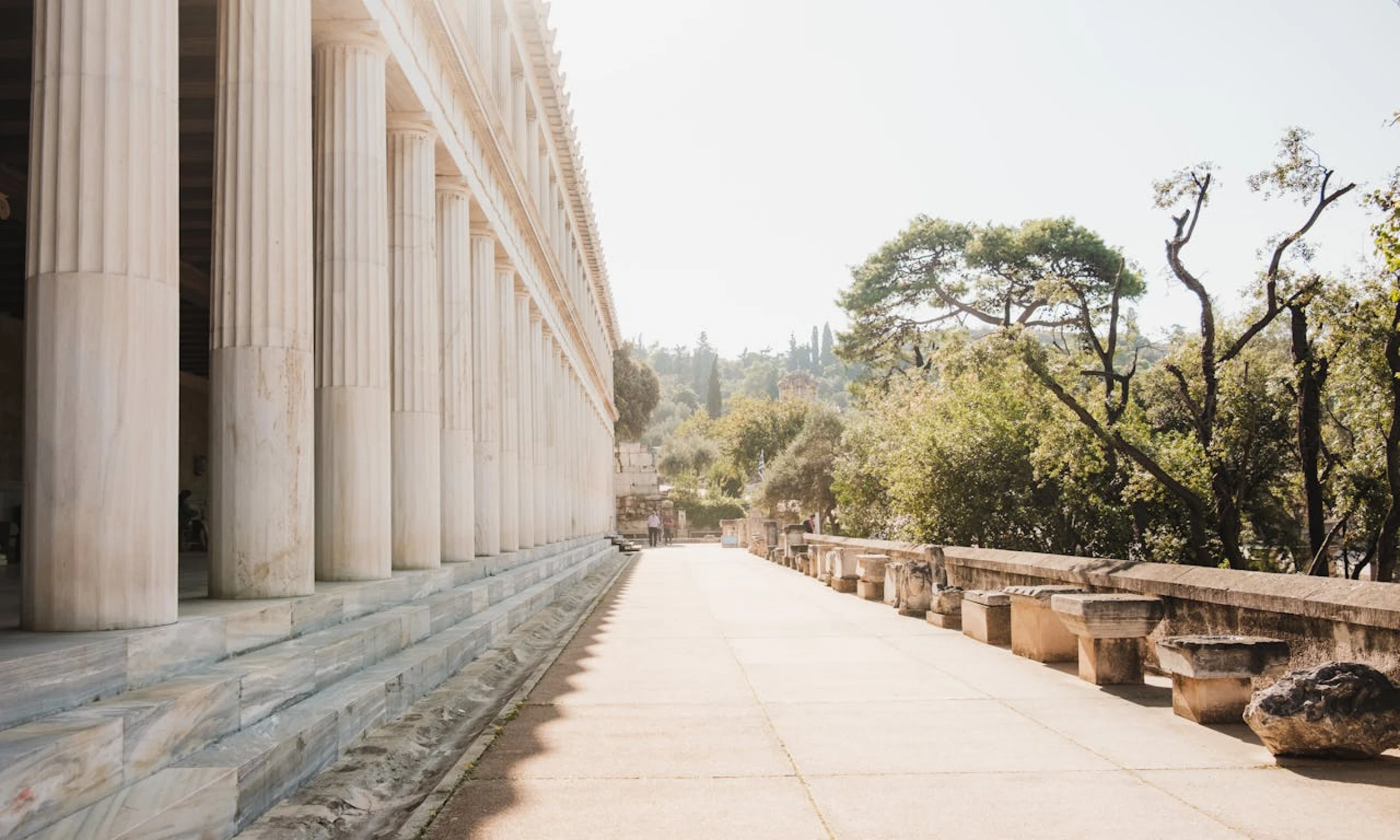 Image of the Stoa of Attalos in Athens, showcasing its long row of marble columns and shaded walkway, with greenery in the background.