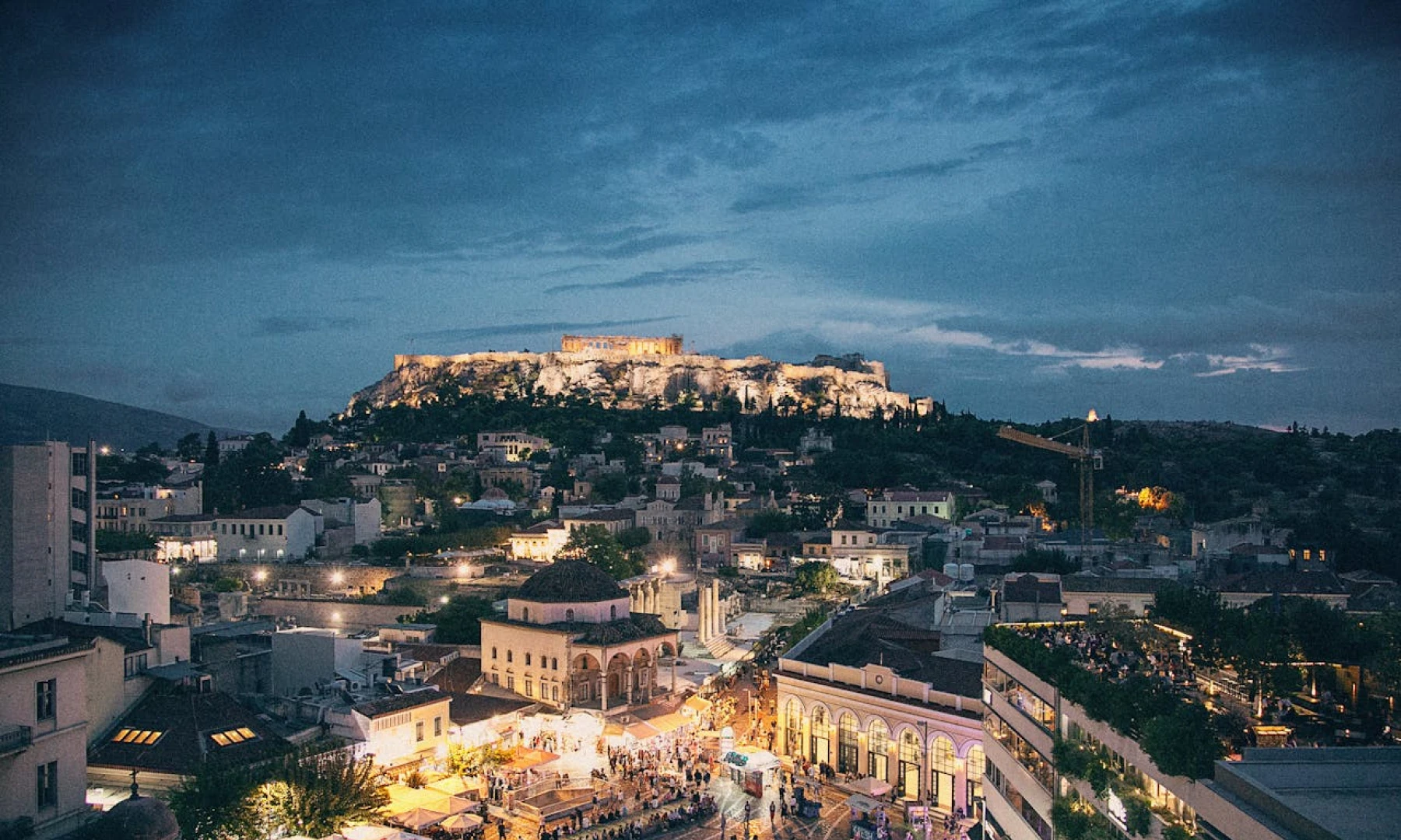 Image of the Acropolis illuminated at night under a dark, cloudy sky in Athens, Greece. This is one of the top sights to experience on a long layover in Athens.