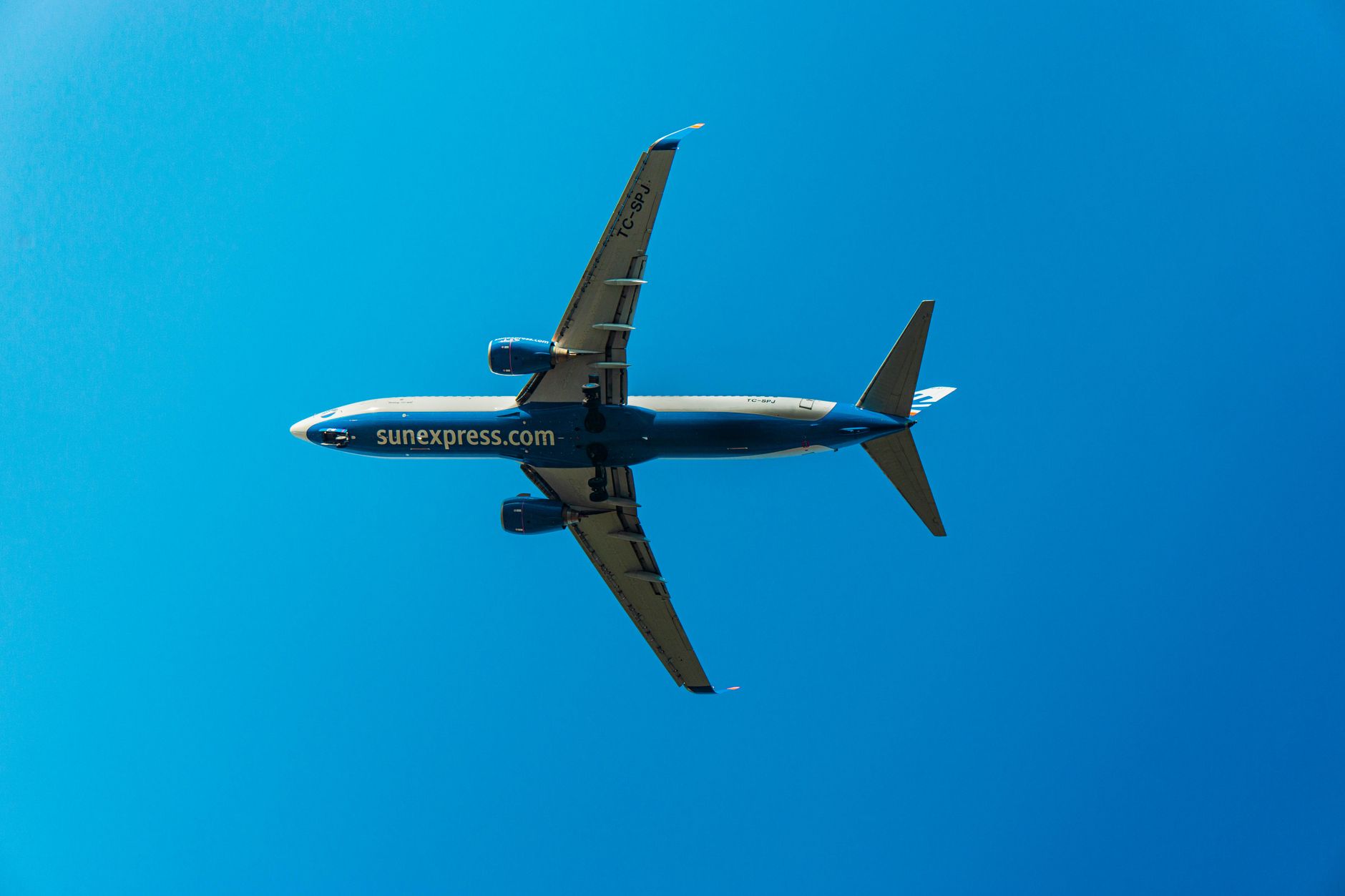 Commercial jet flying overhead against a bright blue sky, captured from below.