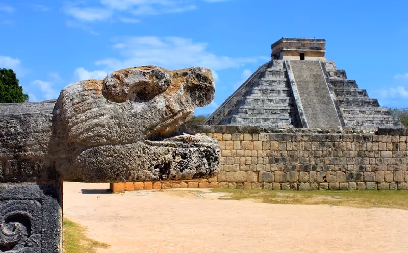 Détail sculpté d’un serpent en pierre avec la pyramide de Chichén Itzá en arrière-plan, site archéologique emblématique du Yucatán.