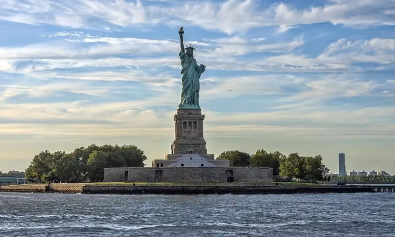 La Statue de la Liberté se dressant majestueusement sur Liberty Island sous un ciel partiellement nuageux.