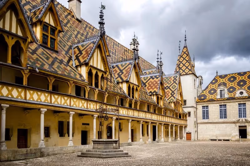 Les toits colorés des Hospices de Beaune sous un ciel orageux.