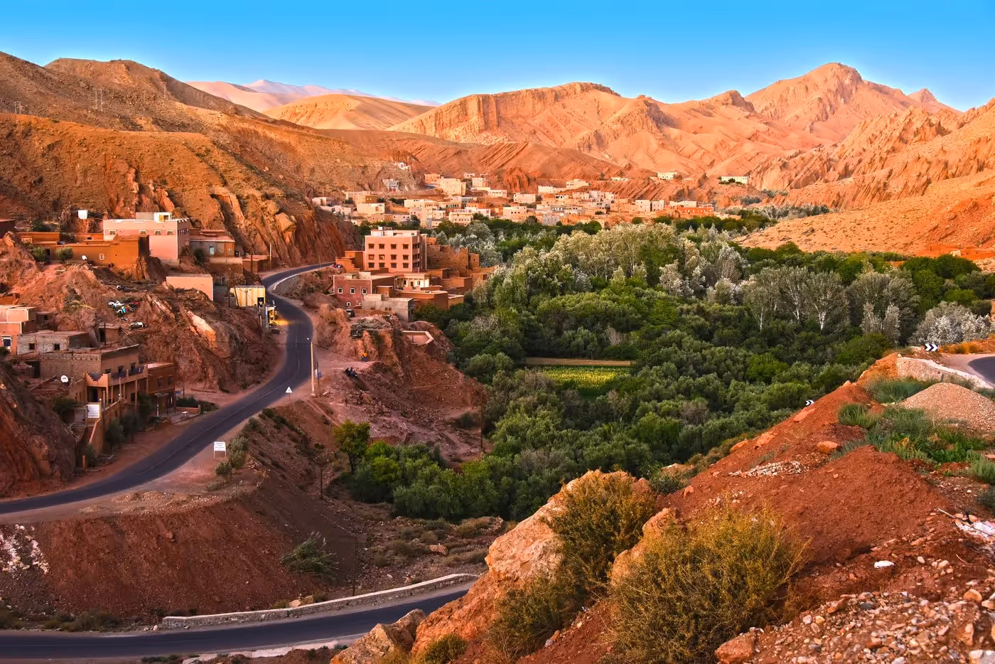 Vue panoramique d’un village marocain traditionnel niché entre des montagnes arides et une vallée verdoyante, au cœur d’une oasis.