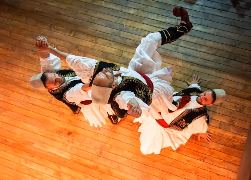 Danseurs albanais en costume traditionnel exécutant une danse folklorique sur une scène en bois