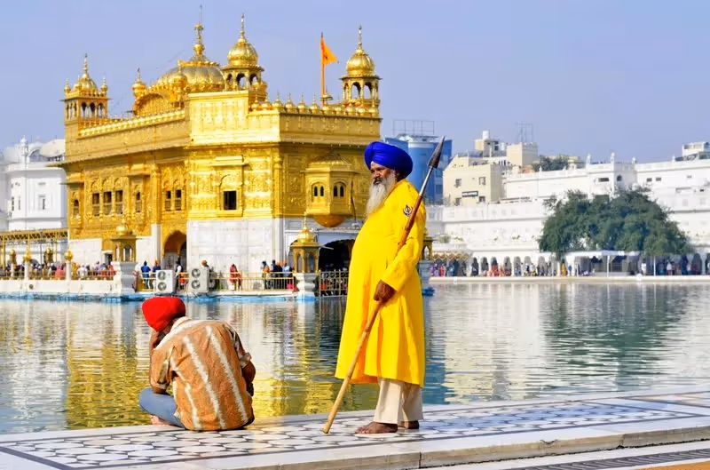 Garde sikh en habit traditionnel devant le Temple d’Or à Amritsar, avec un pèlerin assis au bord du bassin sacré.