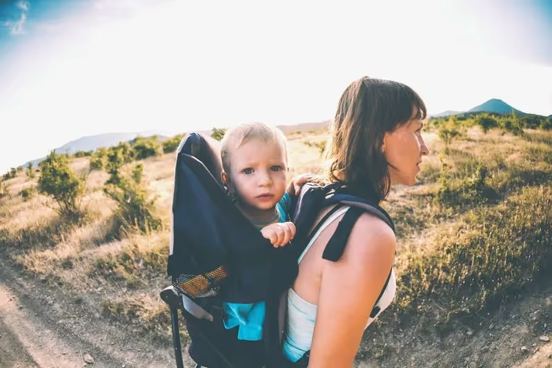 Maman portant son bébé en porte-bébé dorsal lors d’une randonnée sous le soleil