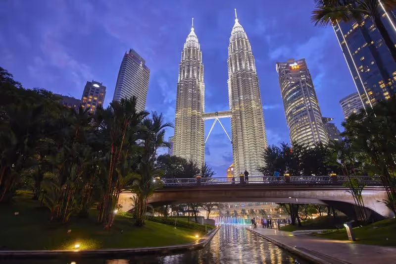 Les tours jumelles Petronas illuminées à la tombée de la nuit à Kuala Lumpur, entourées de gratte-ciels modernes.