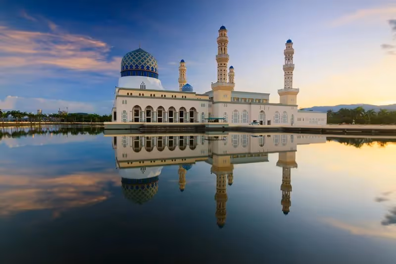 Vue panoramique d'une mosquée au bord d'un lac au coucher du soleil, avec reflets parfaits dans l'eau calme.