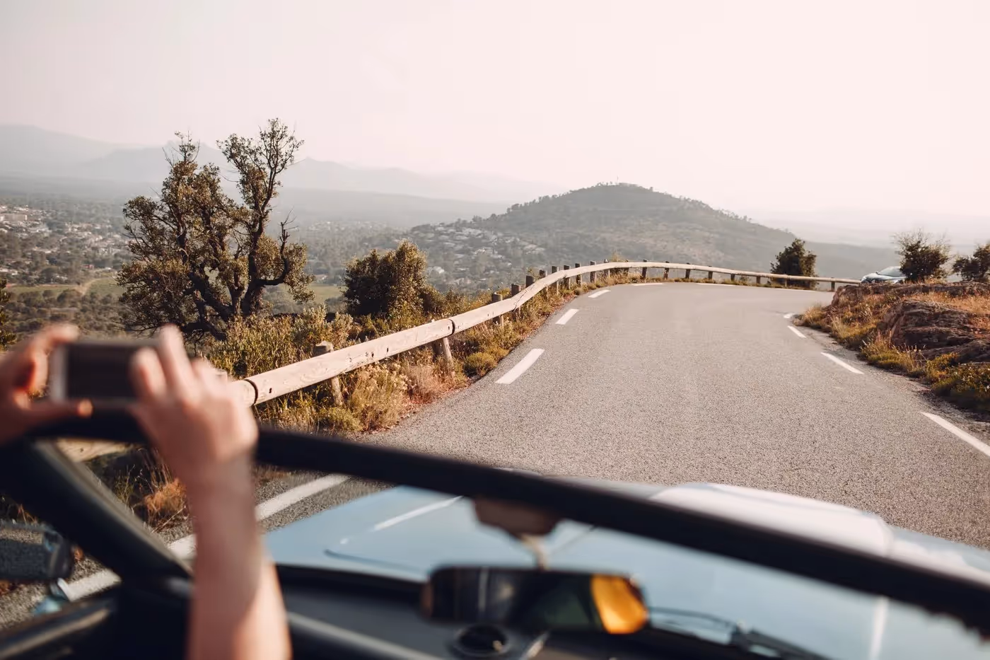 Vue depuis une voiture décapotable sur une route de campagne sinueuse en France, avec collines et végétation typiquement méditerranéenne à l’arrière-plan.